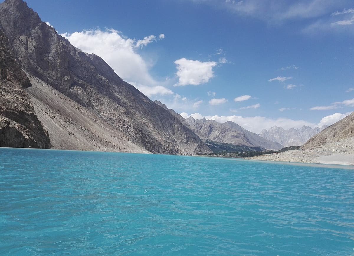 Turquoise water of Attabad Lake filling the gorge below grey scree slopes and a blue sky