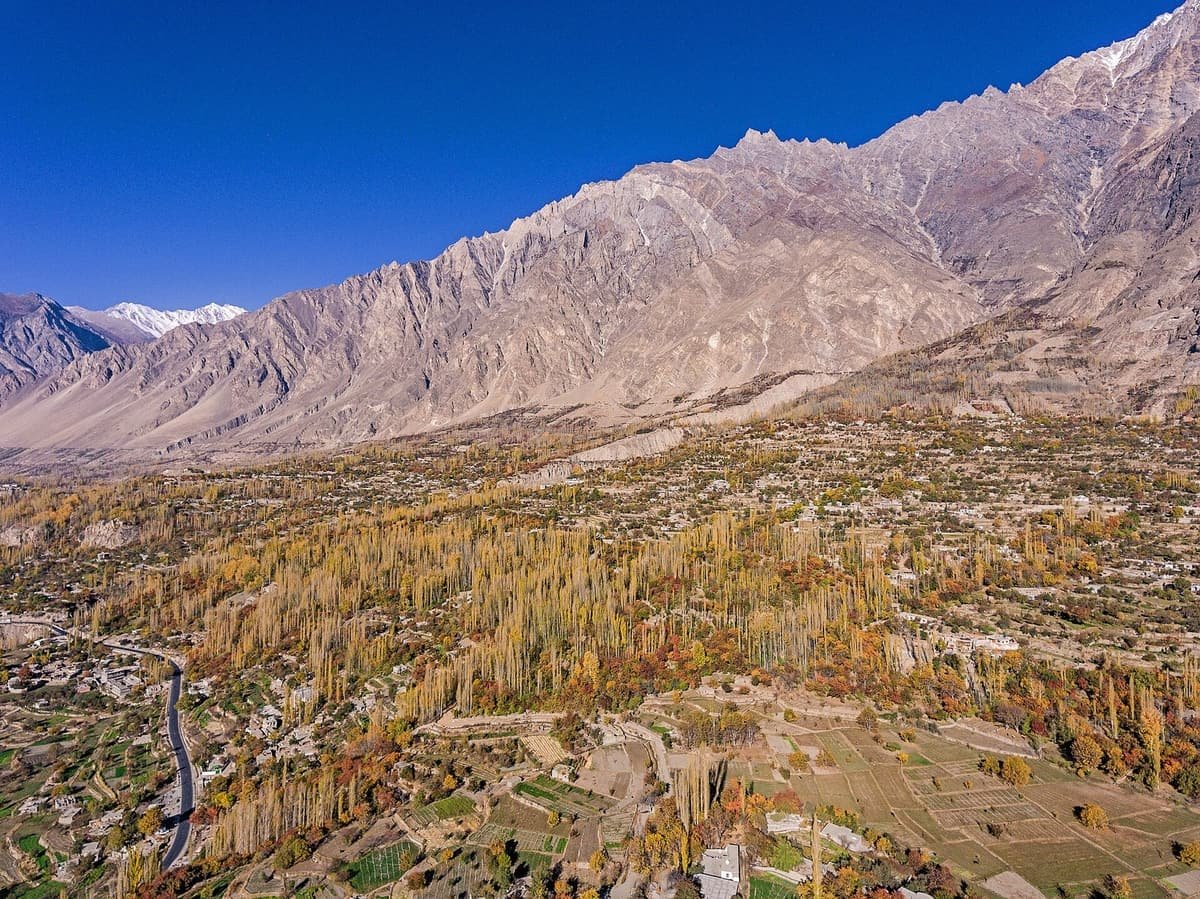 Aerial view of Karimabad's autumn poplars, terraced fields and houses below a long jagged mountain ridge.