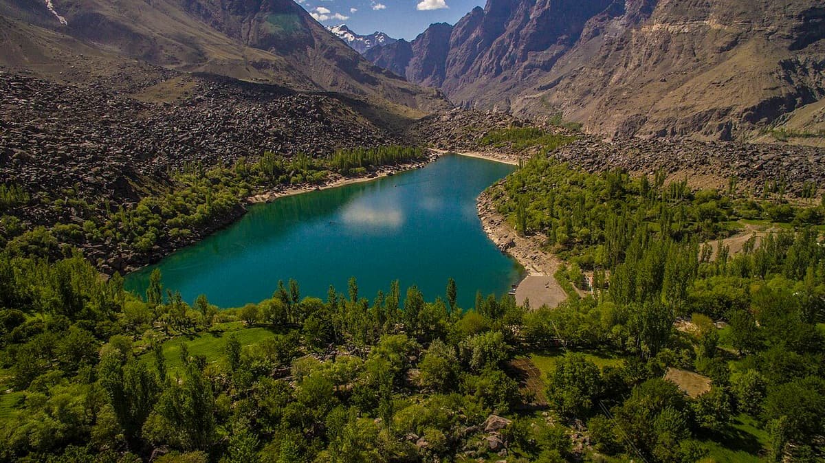 Upper Kachura Lake from above, a deep blue pool ringed by green trees below bare, rocky mountains