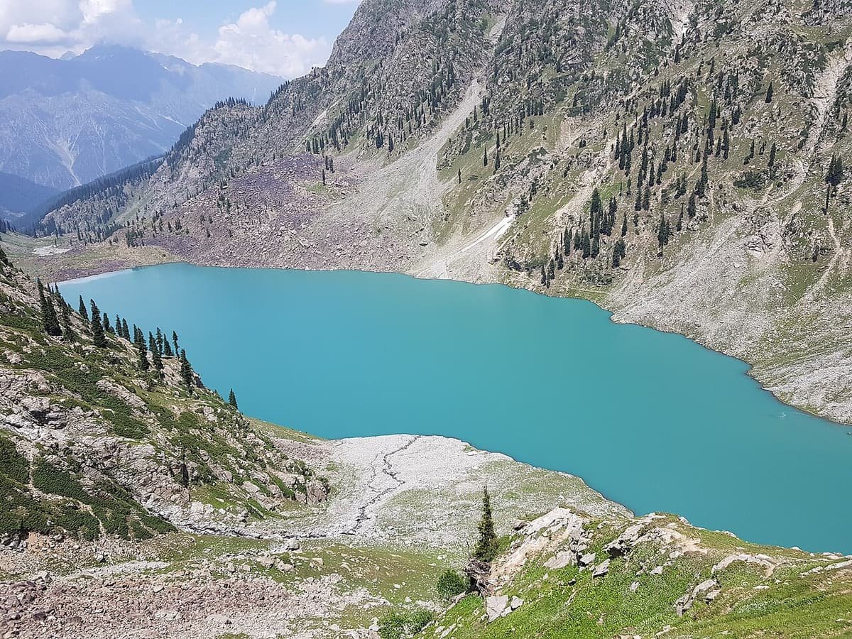 Turquoise Kundol Lake in a high valley of pine-dotted slopes, seen from the hillside above