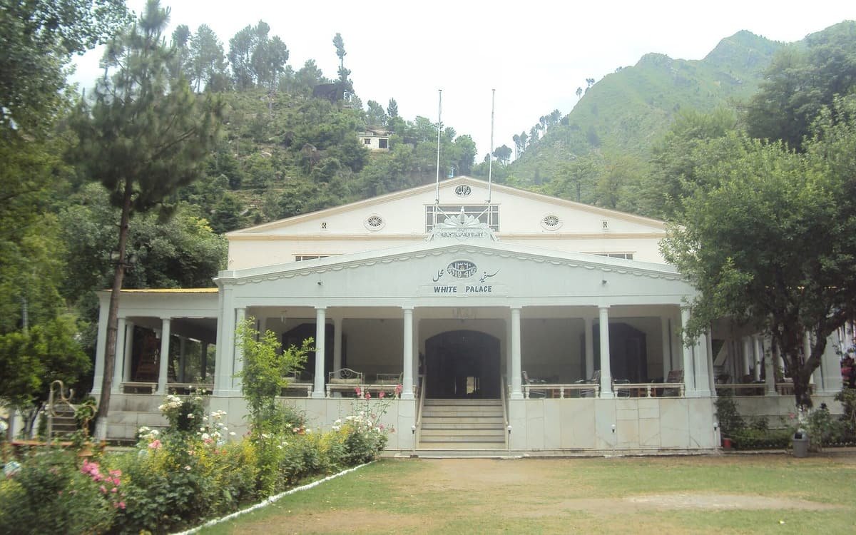 The white columned facade of the 1941 White Palace at Marghazar, with rose beds and a lawn in front of wooded hills.